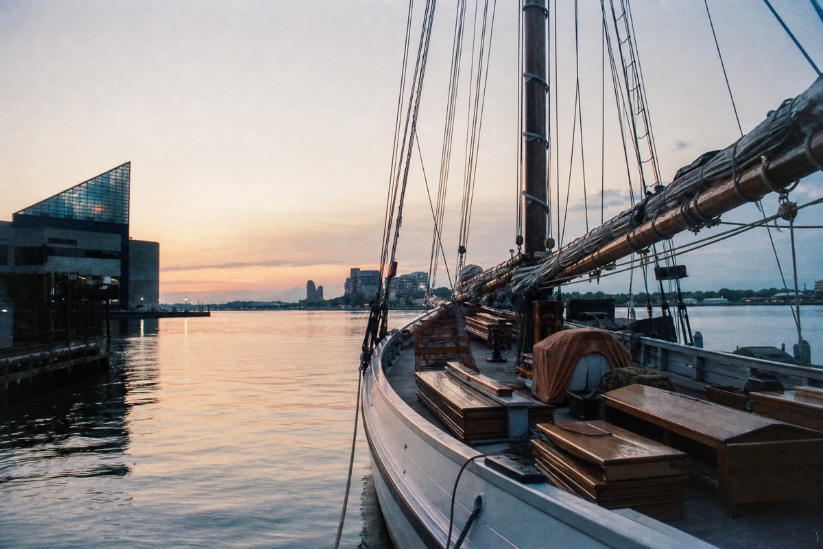 A wooden schooner at anchor alone in a quiet corner of the harbor at dusk, empty deck benches and still water around it