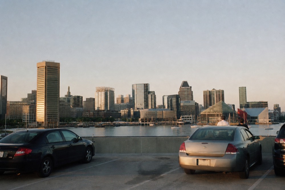 The upper deck of an open parking structure overlooking the harbor, parked cars in the foreground and the downtown skyline and water beyond under afternoon light