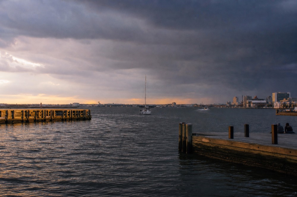 A summer thunderstorm building in dark clouds over the Patapsco River, choppy grey water and a distant boat heading back toward the harbor